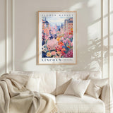 a framed poster of a colorful floral scene hanging on a wall above a white couch with a blanket draped over it.