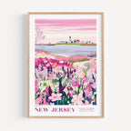 A framed poster depicting a scenic landscape with a lighthouse, a small town, and a field of colorful flowers.