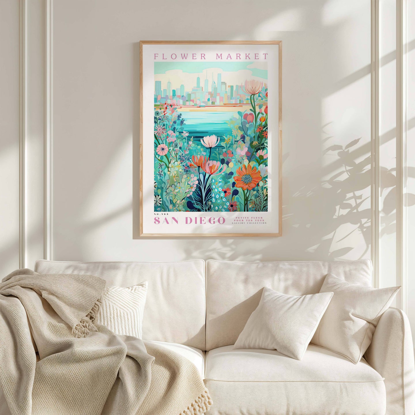 a framed poster of a colorful floral scene hanging on a wall above a white couch with a blanket draped over it.