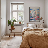 a cozy bedroom with a large bed, a wooden nightstand, and a potted plant. The room has a window with a view of a city, and a framed poster of a flower market is displayed on the wall.