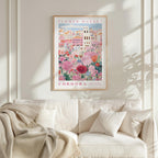 a framed poster of a colorful floral scene hanging on a wall above a white couch with pillows.