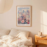 a framed poster of a cityscape with flowers hanging on a wall above a bed with striped pillows.