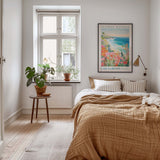 A cozy bedroom with a large bed, a nightstand with a plant, and a framed poster of a beach scene on the wall.