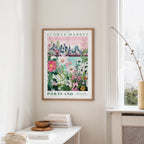 a framed poster of a cityscape with a flower market in Portland, Oregon, hanging on a wall.