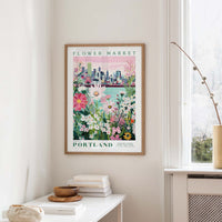 a framed poster of a cityscape with a flower market in Portland, Oregon, hanging on a wall.