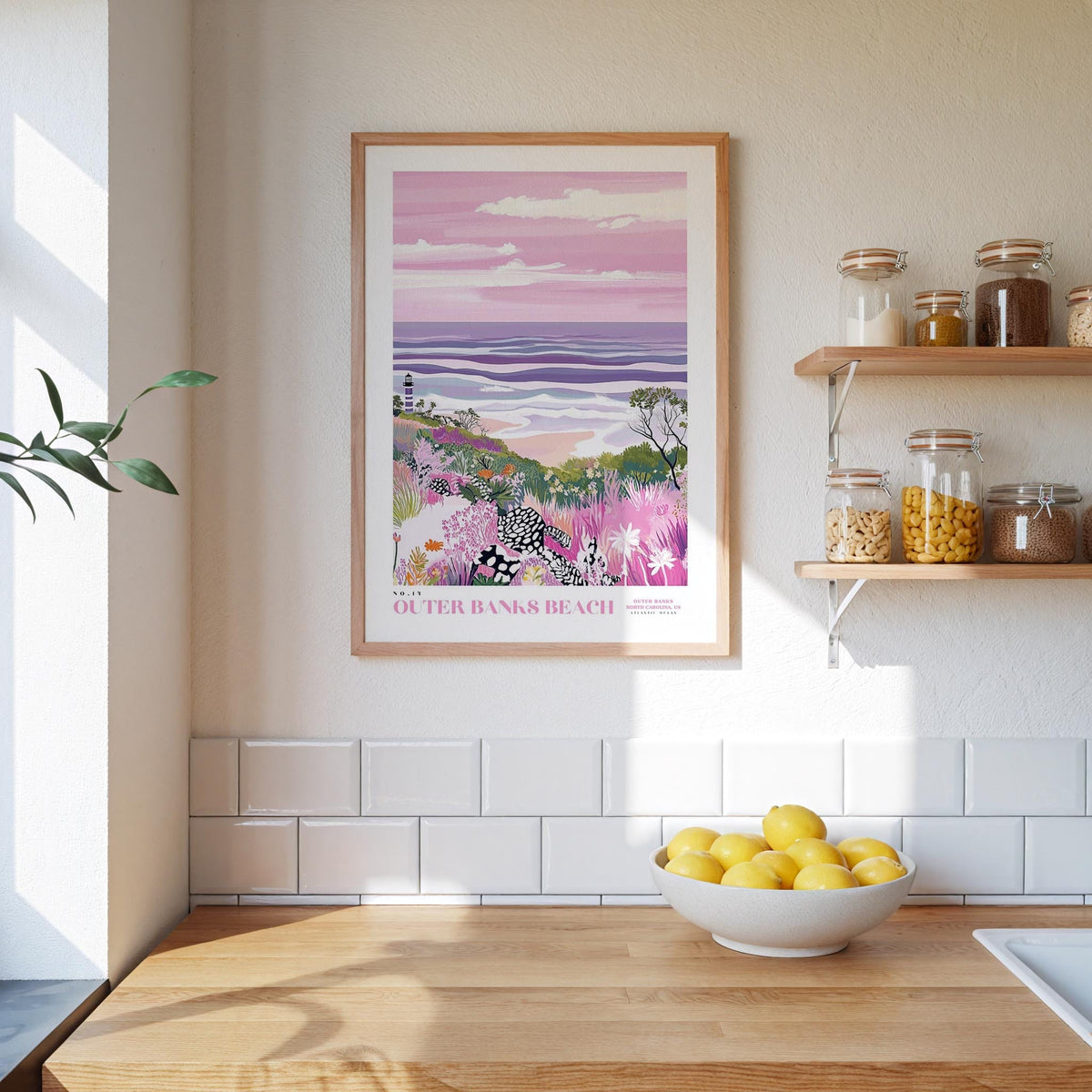 a kitchen counter with a bowl of lemons, a framed picture of a beach scene, and a shelf with jars and bottles.