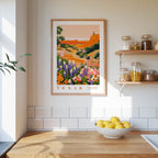 a framed poster of a colorful landscape of flowers hanging on a wall above a wooden countertop with a bowl of lemons.
