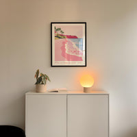 a framed poster of a beach scene with palm trees, a potted plant, and a lamp on a white cabinet.
