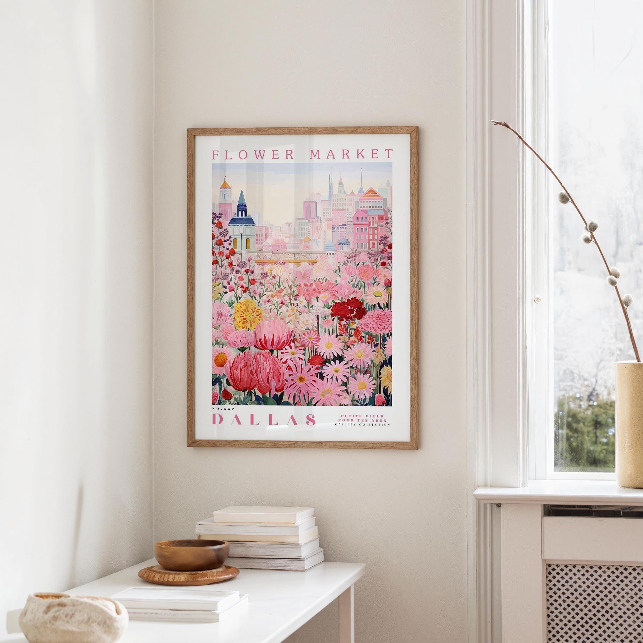 a framed poster of a colorful floral scene hanging on a wall, with a white table and a vase of flowers in the foreground.