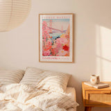 a bedroom scene with a framed poster of a flower market in San Francisco hanging on the wall above a bed with striped pillows.
