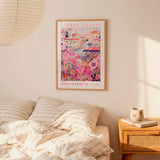 a bedroom setting with a framed poster of a flower market hanging on the wall above a bed with striped pillows.