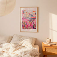 a bedroom setting with a framed poster of a flower market hanging on the wall above a bed with striped pillows.