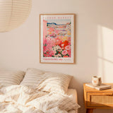 a bedroom scene with a framed poster of a flower market hanging on the wall above a bed with striped pillows.