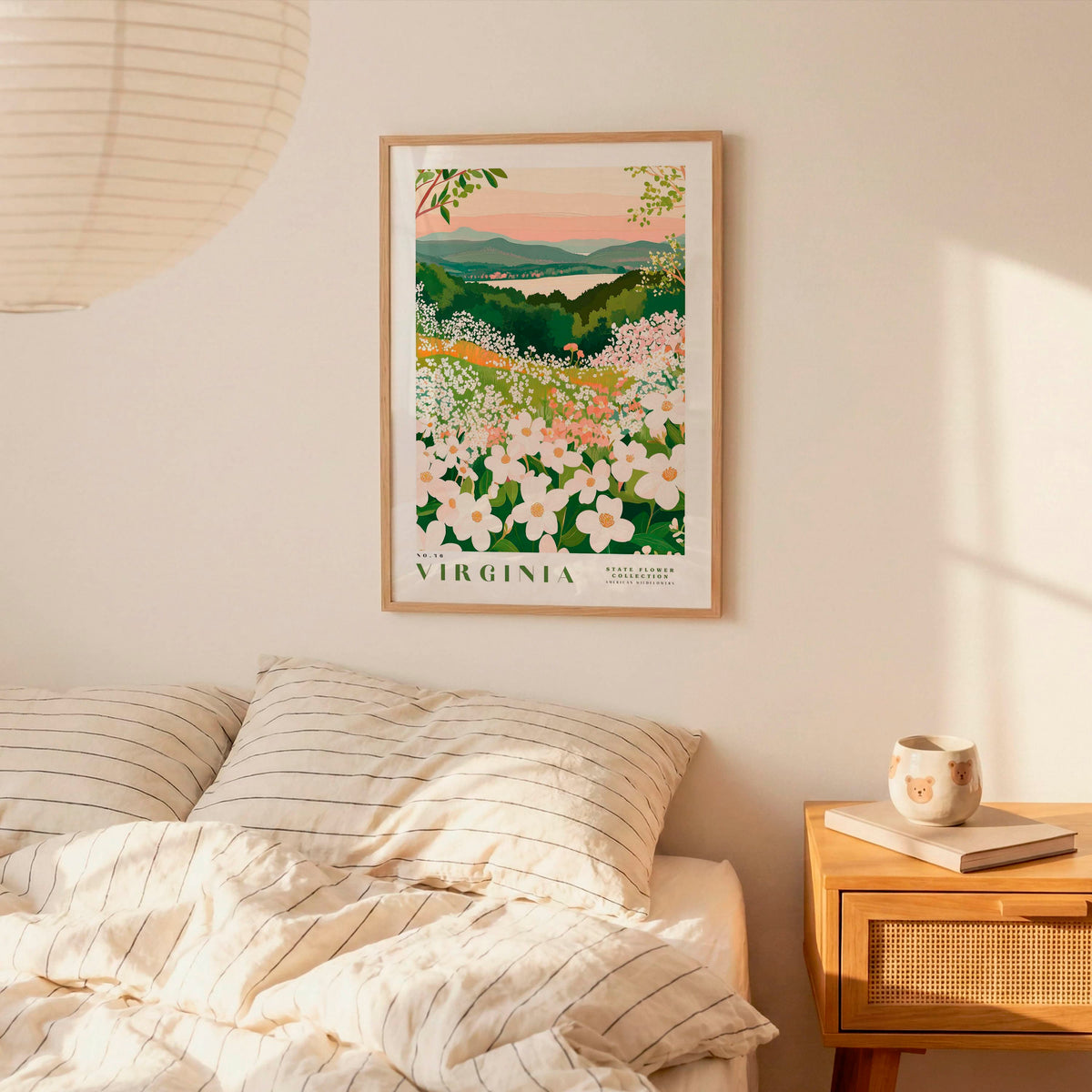 a bedroom scene with a framed poster of a floral landscape hanging on the wall above a bed with striped pillows.