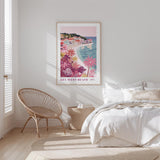 a bedroom with a large poster of a beach scene hanging on the wall, a wicker chair, and a bed with white bedding.