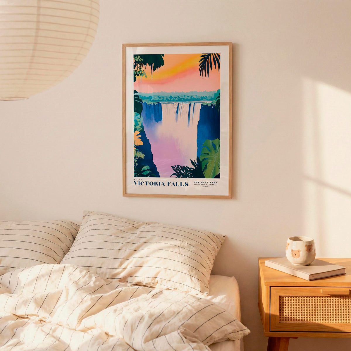 a bedroom scene with a framed poster of Victoria Falls hanging on the wall above a bed with striped pillows.