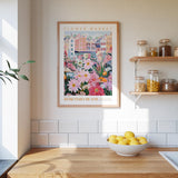 a kitchen scene with a framed poster of a colorful floral market on the wall above a wooden countertop with a bowl of lemons.