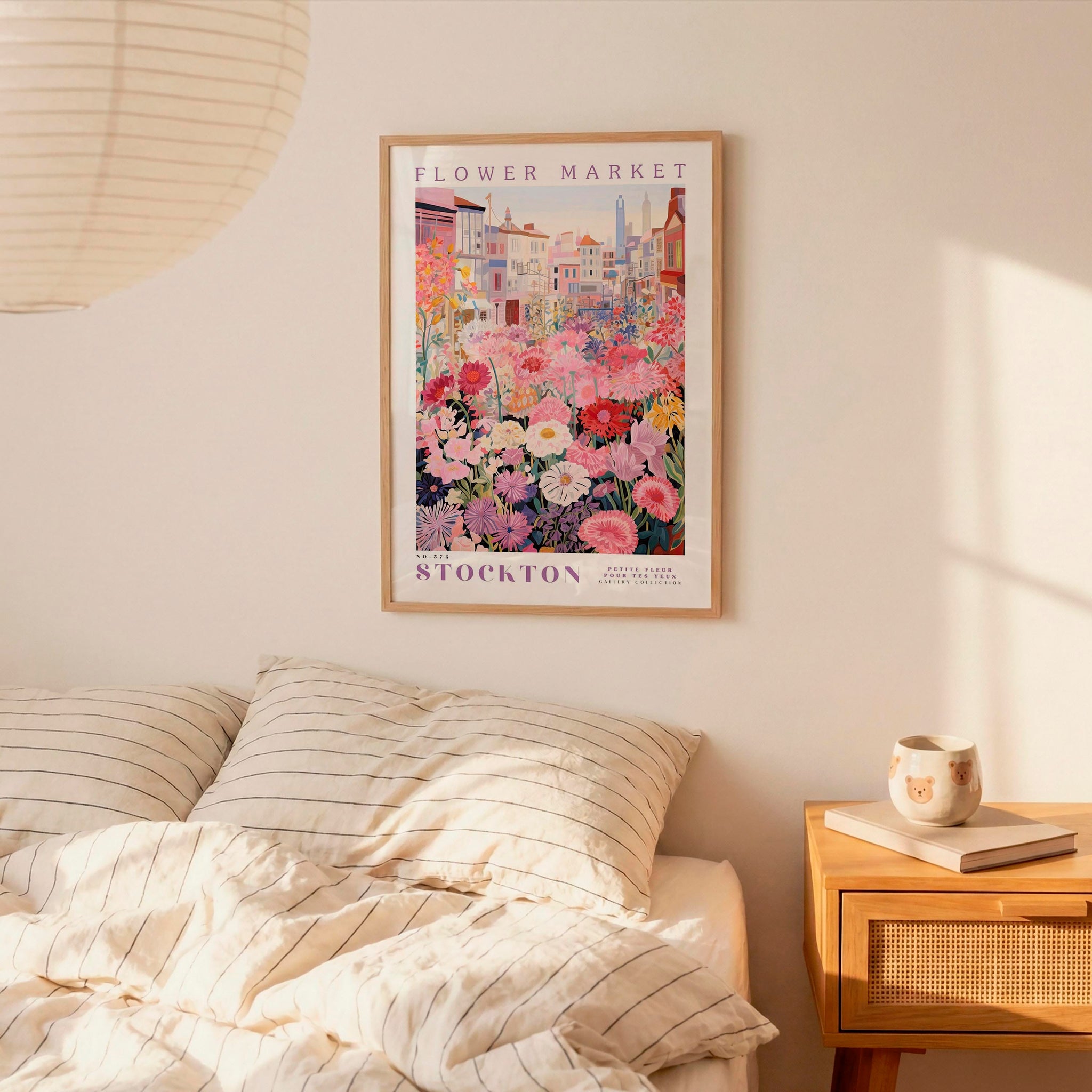 a bedroom scene with a framed poster of a flower market hanging on the wall above a bed with striped pillows.