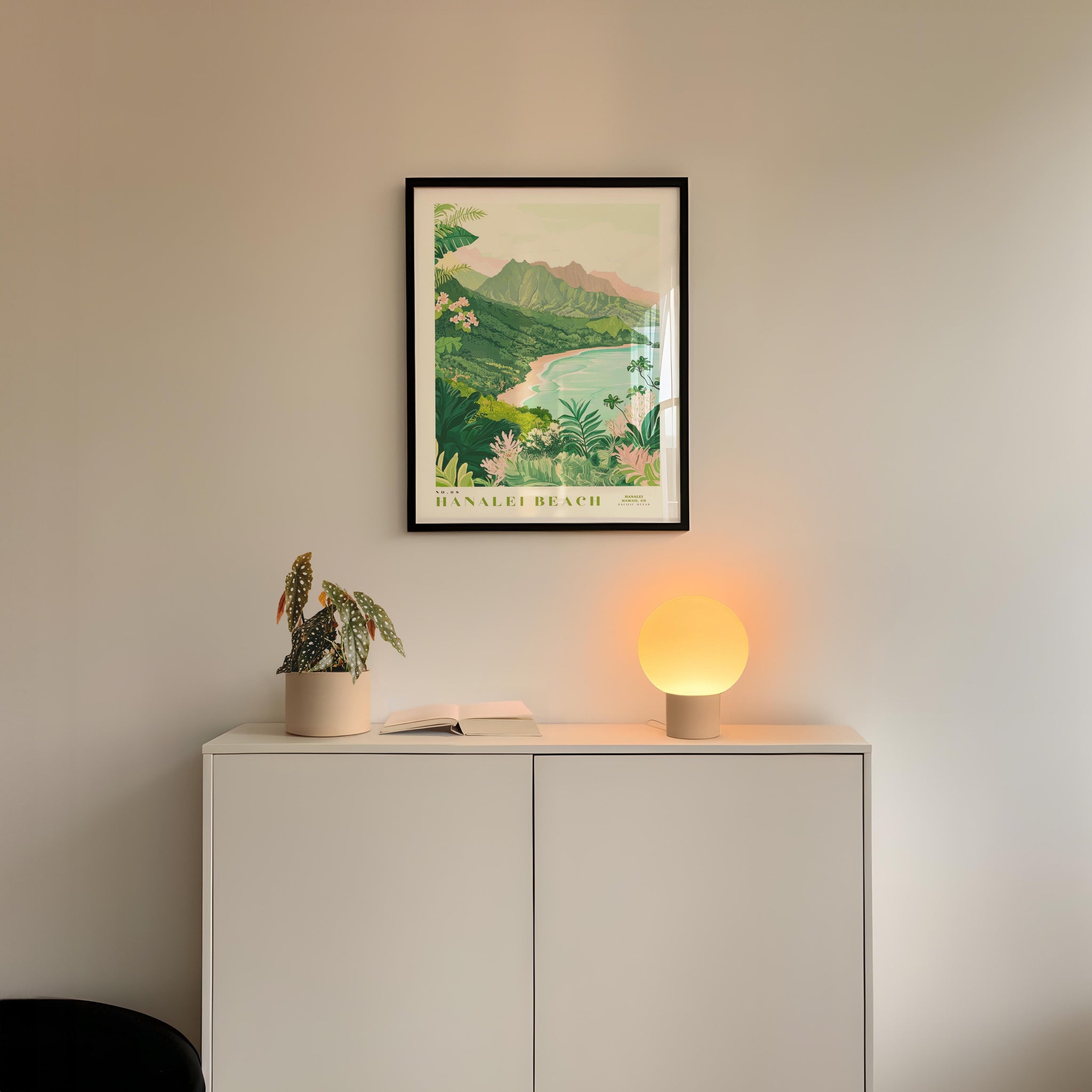 a framed poster of a tropical beach landscape hanging on a wall above a white cabinet with a plant and a lamp on top.