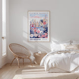a bedroom with a large poster of Melbourne's Flower Market hanging on the wall, a wicker chair, and a bed with white bedding.