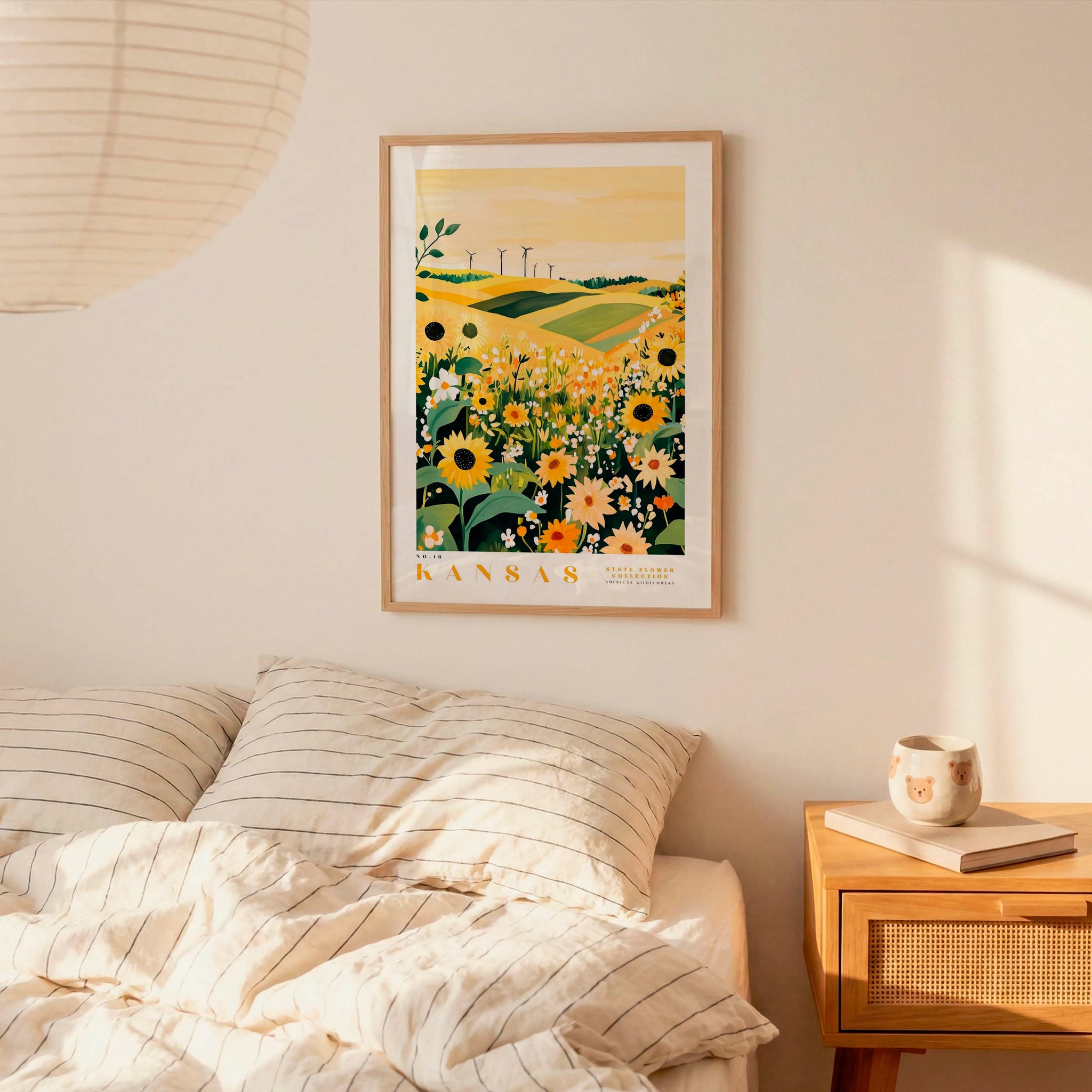 a bedroom scene with a framed poster of a field of flowers hanging on the wall above a bed with striped pillows.
