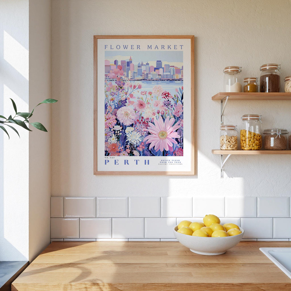 a kitchen counter with a bowl of lemons, a framed poster of a flower market in Perth, and a shelf with jars and containers.