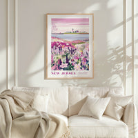 a framed poster of a scenic landscape with a field of flowers and a body of water, hanging on a wall above a white couch with a blanket draped over it.