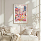 a framed poster of a flower market in Memphis, Tennessee, hanging on a white wall above a white couch with a blanket draped over it.
