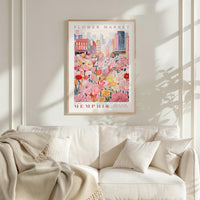 a framed poster of a flower market in Memphis, Tennessee, hanging on a white wall above a white couch with a blanket draped over it.