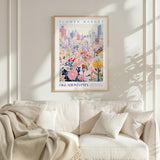 a framed poster of a cityscape with a flower market in the background, hanging on a wall above a white couch with a blanket draped over it.