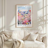 a framed poster of a colorful floral scene hanging on a wall above a white couch with a blanket draped over it.