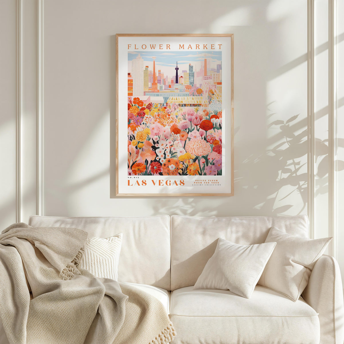 a framed poster of a cityscape with a flower market in the background, hanging on a wall above a white couch with pillows.