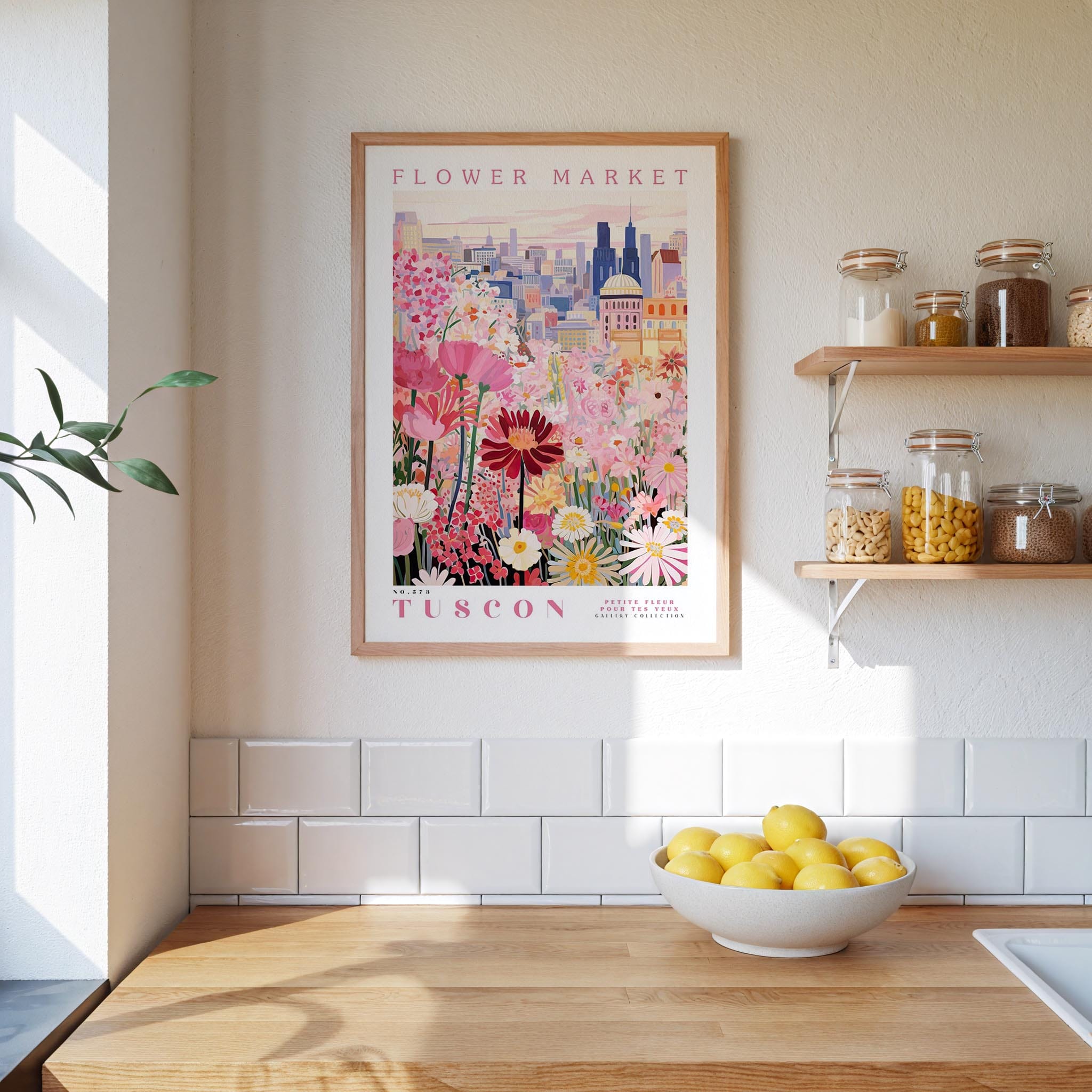 a framed poster of a colorful floral scene hanging on a wall above a kitchen counter with a bowl of lemons on it.
