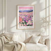 a framed poster of a field of flowers, with mountains in the background, hanging on a wall above a white couch.