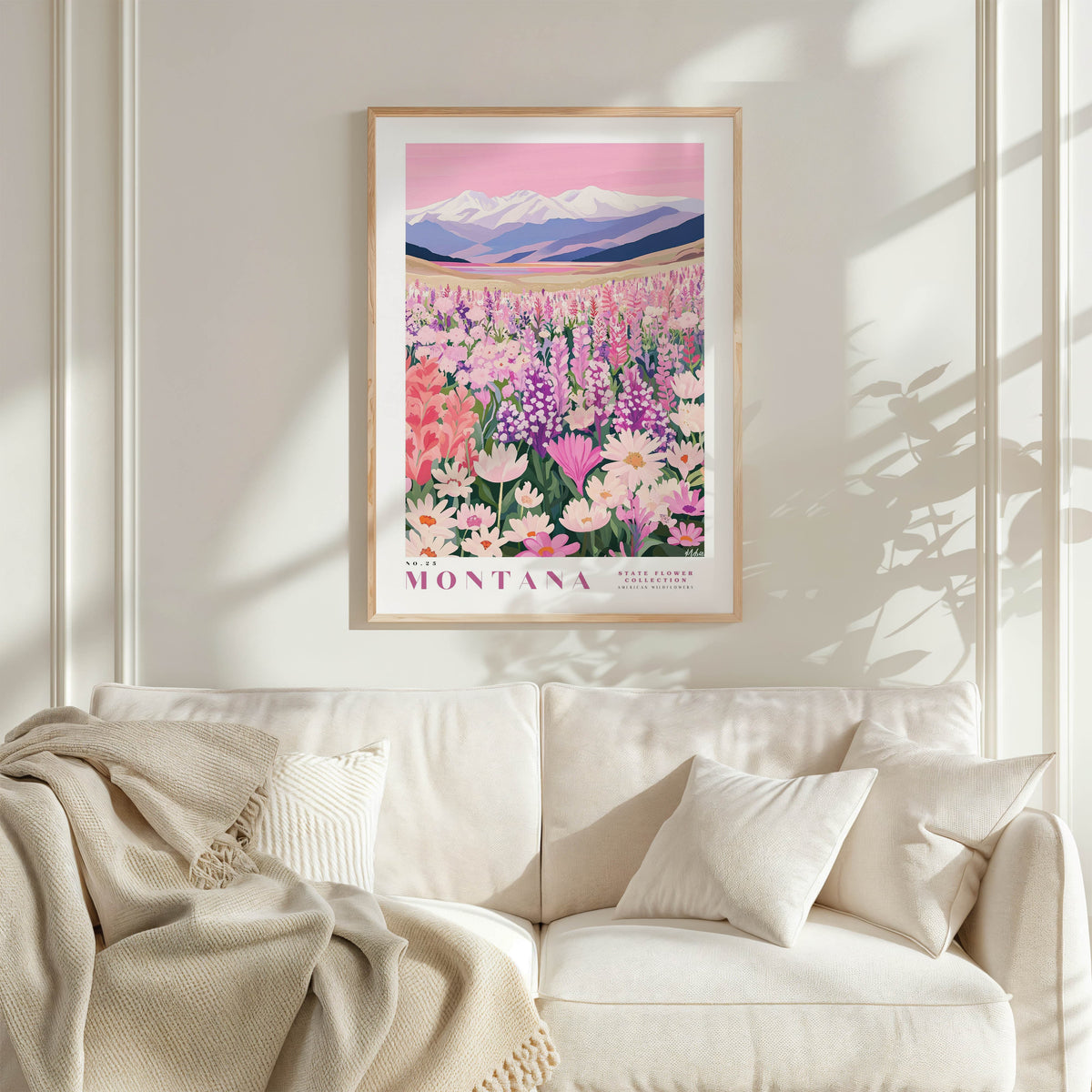 a framed poster of a field of flowers, with mountains in the background, hanging on a wall above a white couch.