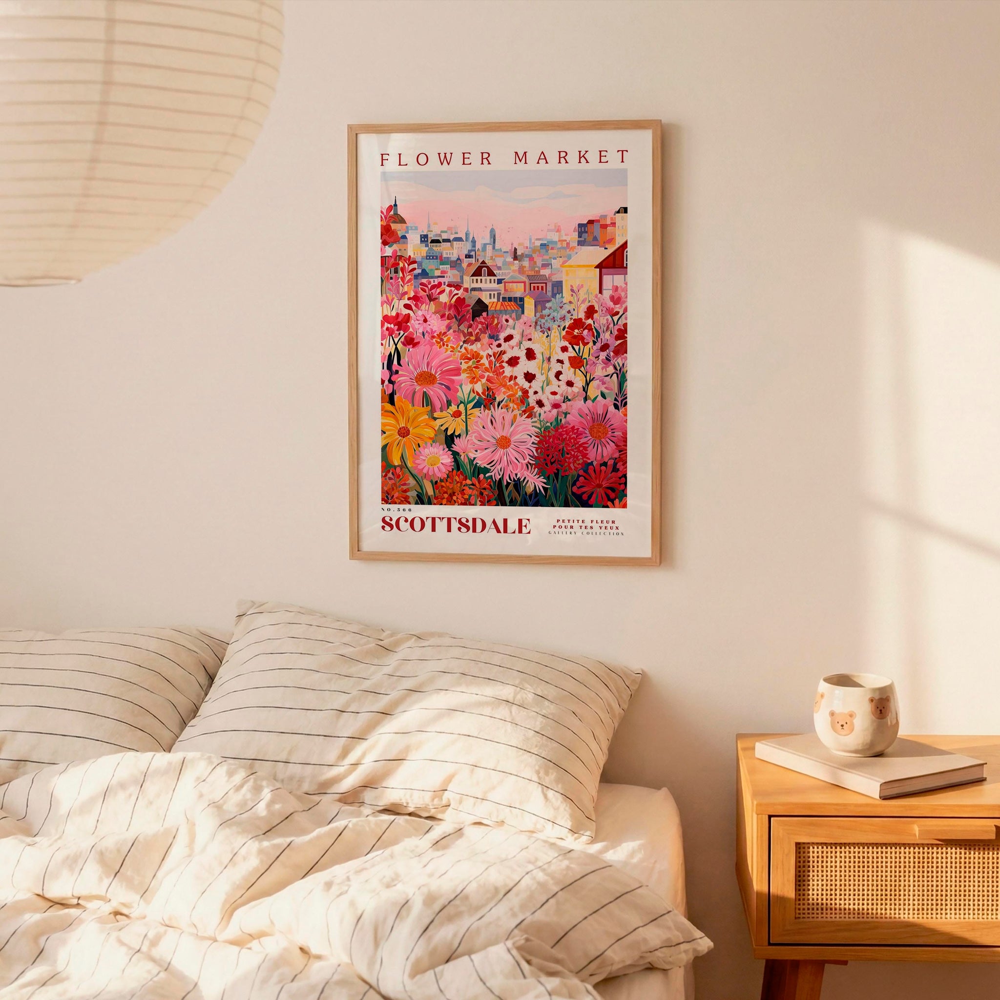 a bedroom setting with a framed poster of a colorful flower market hanging on the wall above a bed with striped pillows.