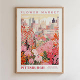 A framed poster depicting a vibrant cityscape with a variety of colorful flowers in the foreground, set against a backdrop of tall buildings.