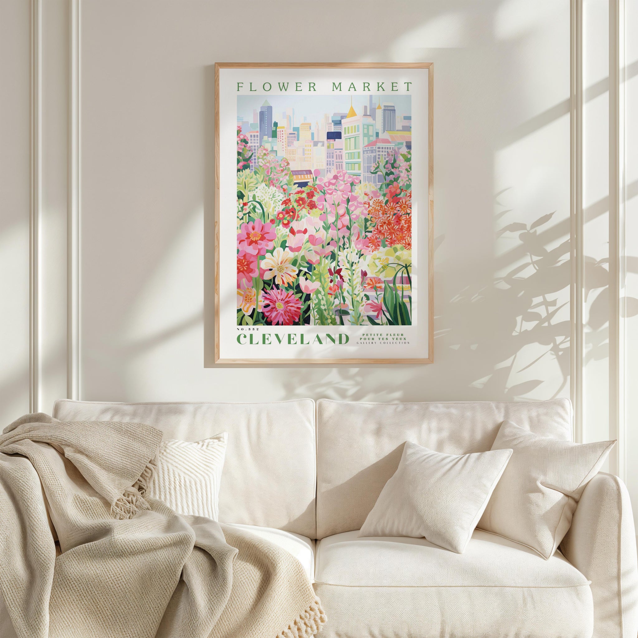 a framed poster of a colorful cityscape with flowers, hanging on a wall above a white couch with pillows.