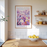 a framed poster of a colorful floral scene hanging on a wall above a wooden countertop with a bowl of lemons.