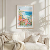 a framed poster of a beach scene with flowers hanging on a wall above a white couch with pillows.