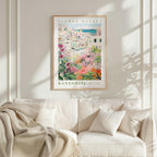 a framed poster of a colorful floral scene hanging on a wall above a white couch with a blanket draped over it.