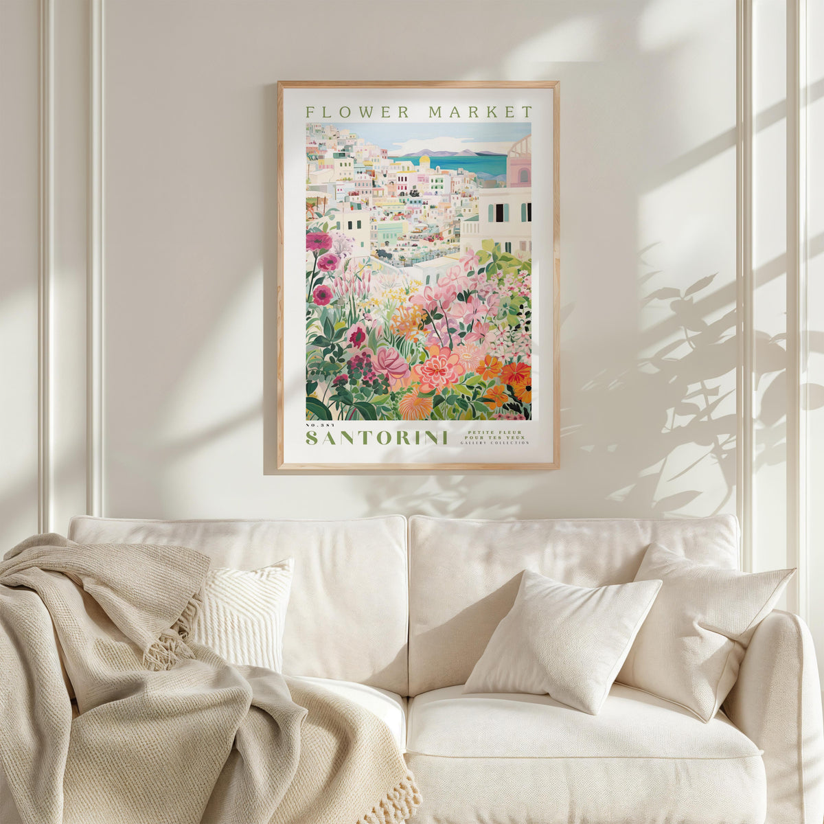 a framed poster of a colorful floral scene hanging on a wall above a white couch with a blanket draped over it.