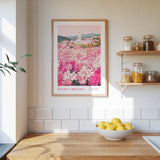 a kitchen counter with a bowl of lemons, a framed poster of a pink flower field, and a shelf with jars and containers.
