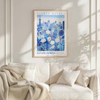 a framed poster of a cityscape with a floral design, hanging on a wall above a white couch with a blanket draped over it.