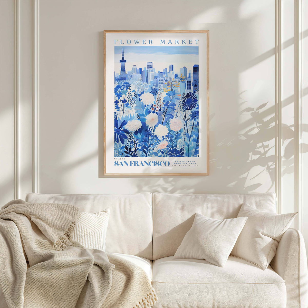 a framed poster of a cityscape with a floral design, hanging on a wall above a white couch with a blanket draped over it.