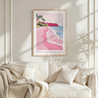 a framed poster of a beach scene with palm trees and pink sand, hanging on a wall above a white couch with a blanket draped over it.