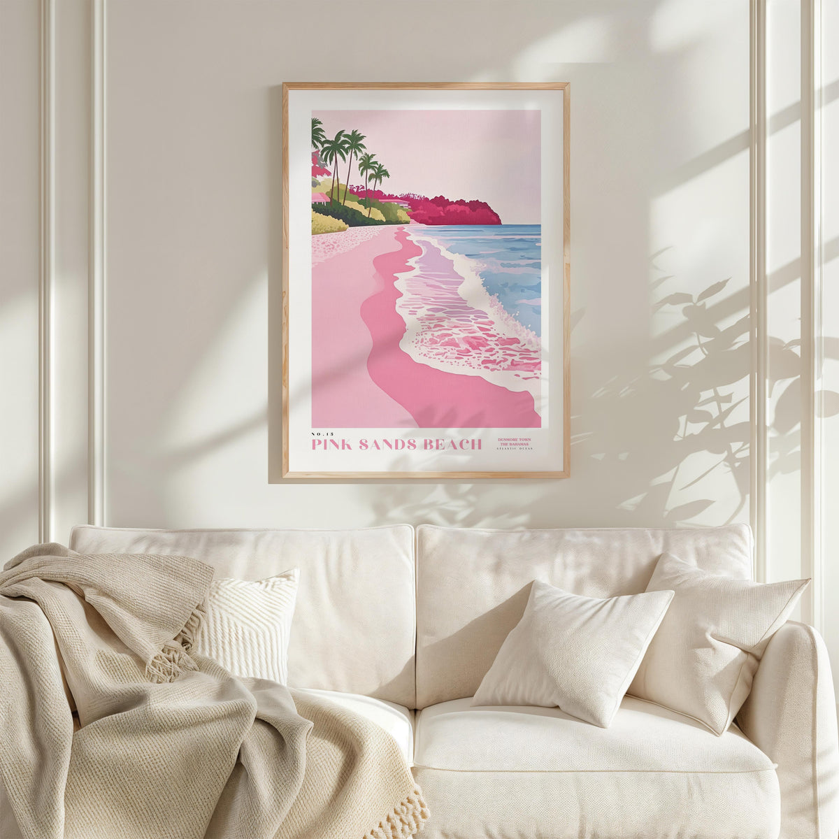 a framed poster of a beach scene with palm trees and pink sand, hanging on a wall above a white couch with a blanket draped over it.