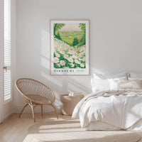 a serene bedroom scene with a large framed poster of a field of flowers hanging on the wall, a woven chair, and a neatly made bed with white bedding.