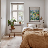 a cozy bedroom with a large bed, a nightstand with a plant, and a framed poster of a field of flowers on the wall.