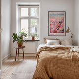 a cozy bedroom with a large bed, a wooden nightstand, and a window with a plant on the sill. The room has a warm, inviting atmosphere with a neutral color palette and natural elements like the potted plant and the rug.